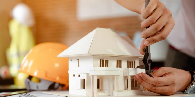 close-up-of-male-architect-hands-measuring-and-making-model-house-on-the-desk-at-sunset-.jpg
